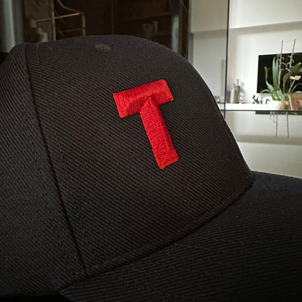 Black cap with a red letter 'T' on a blurred indoor background