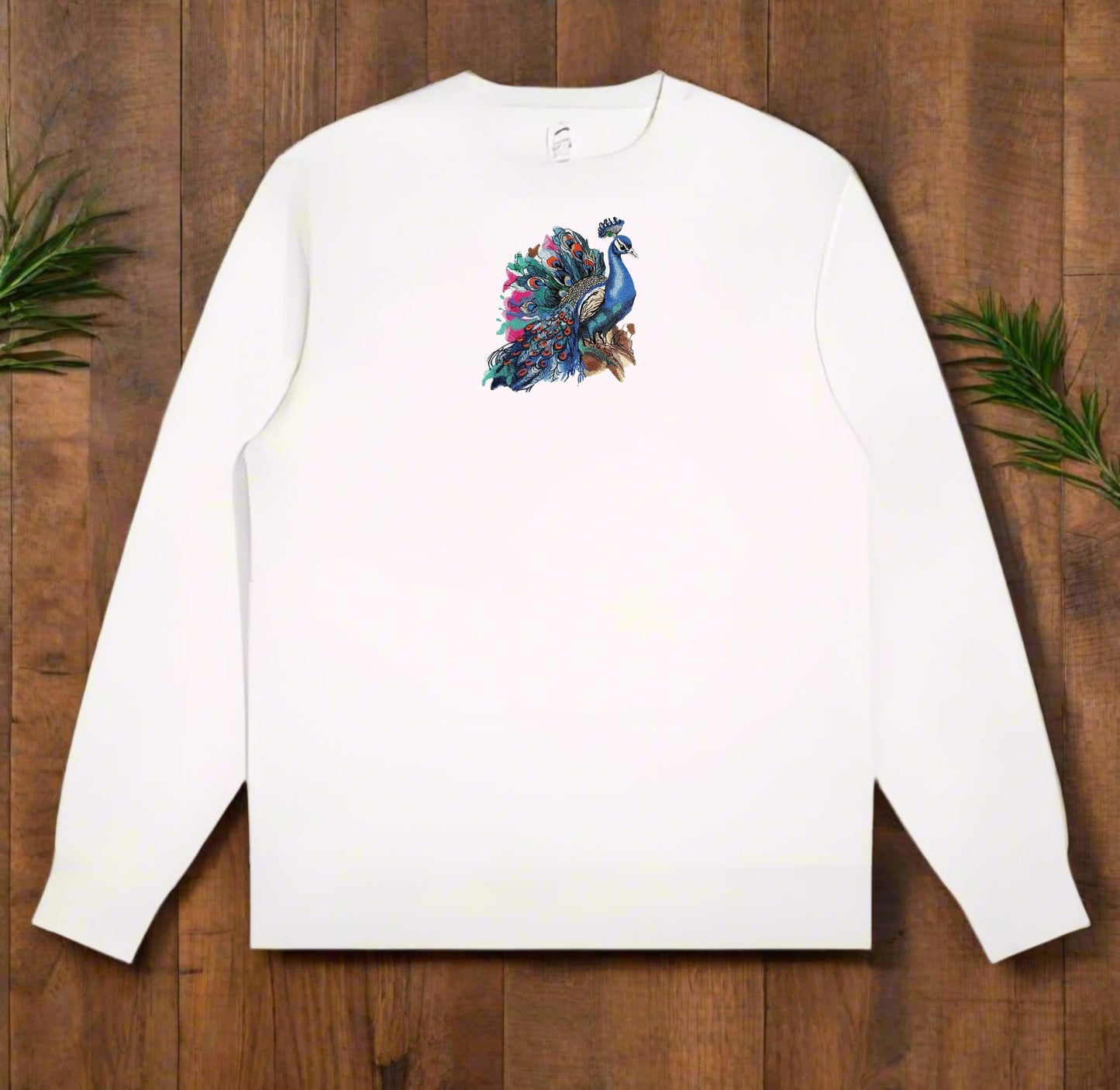 White long-sleeve sweatshirt with a colorful peacock design on a wooden surface.