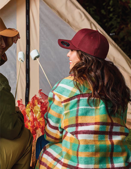 A person wearing a red Flexfit cap with 3D puff embroidery sitting in front of a tent.
