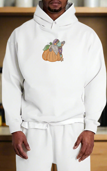 Person wearing a white hoodie with a Pumpkin Gnome Wave Embroidery Design on a wooden shelf background.