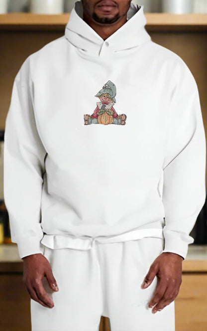 Person wearing a white hoodie with a  Scarecrow Pumpkin Embroidery Design on a wooden shelf background