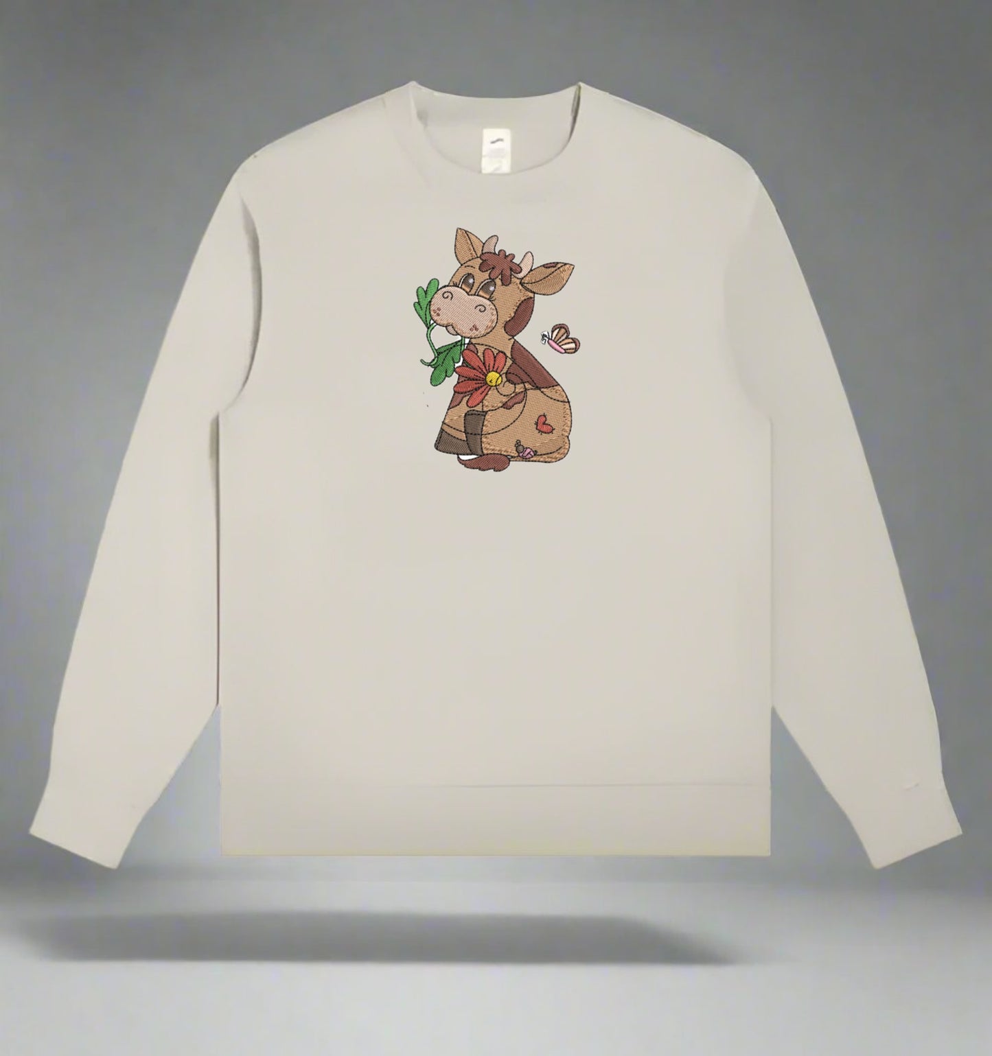 Beige sweatshirt with a cartoon cow design holding flowers on a gray background