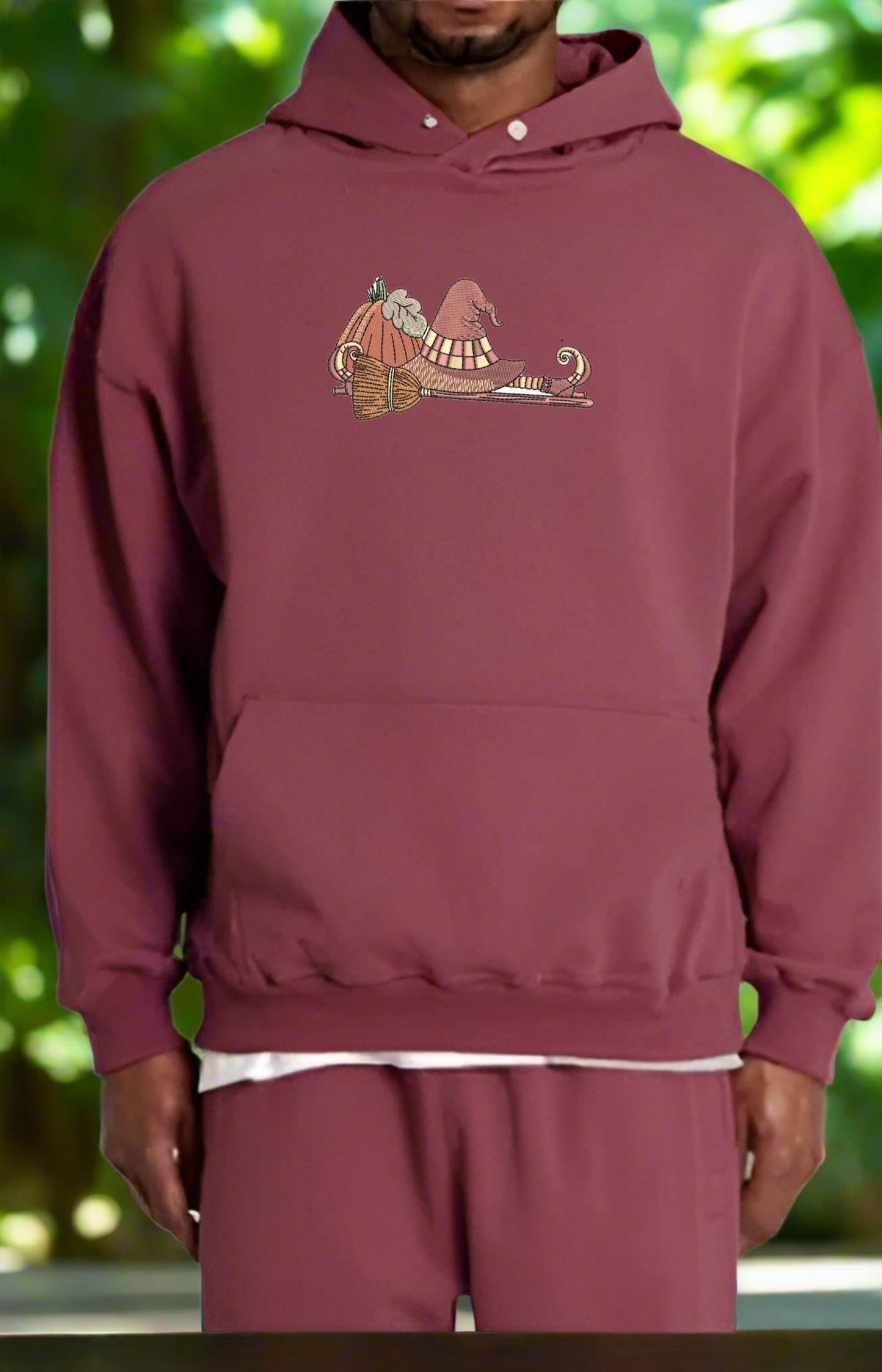 Maroon hoodie with a If the Broom Fits Ride It Embroidery Design on a blurred green background