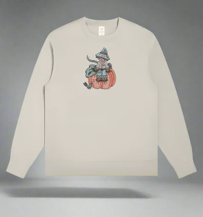 Beige long-sleeve shirt with a graphic of a person in a witch costume on a pumpkin against a gray background.
