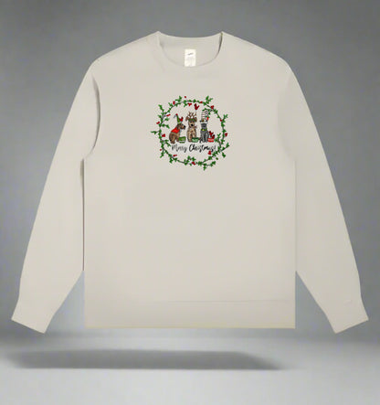Light beige crewneck sweatshirt with an embroidered wreath of holly surrounding three holiday dogs and “Merry Christmas!” text.