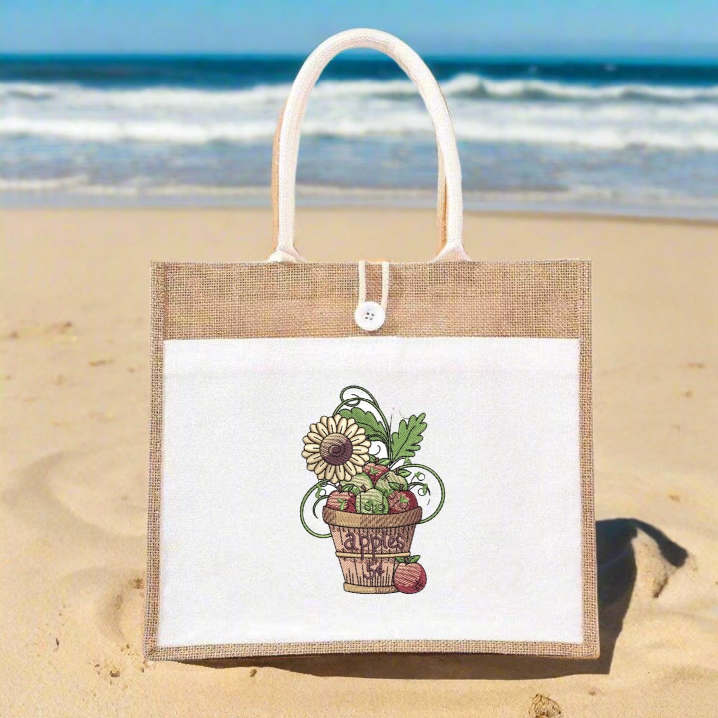 Jute bag with a floral design on a sandy beach with ocean in the background