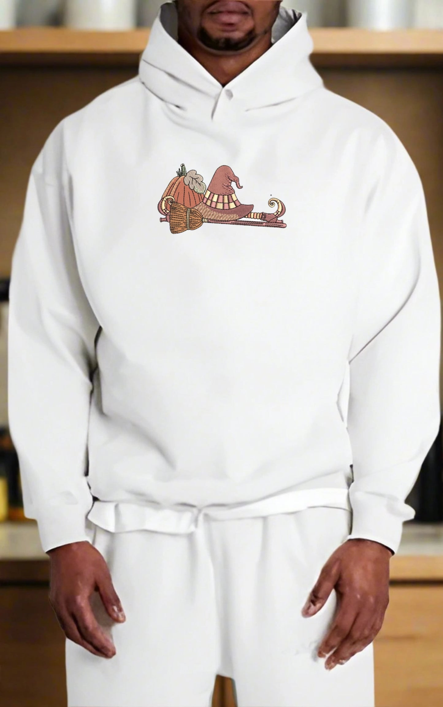 Person wearing a white hoodie with an  If the Broom Fits Ride It Embroidery Design on a wooden shelf background