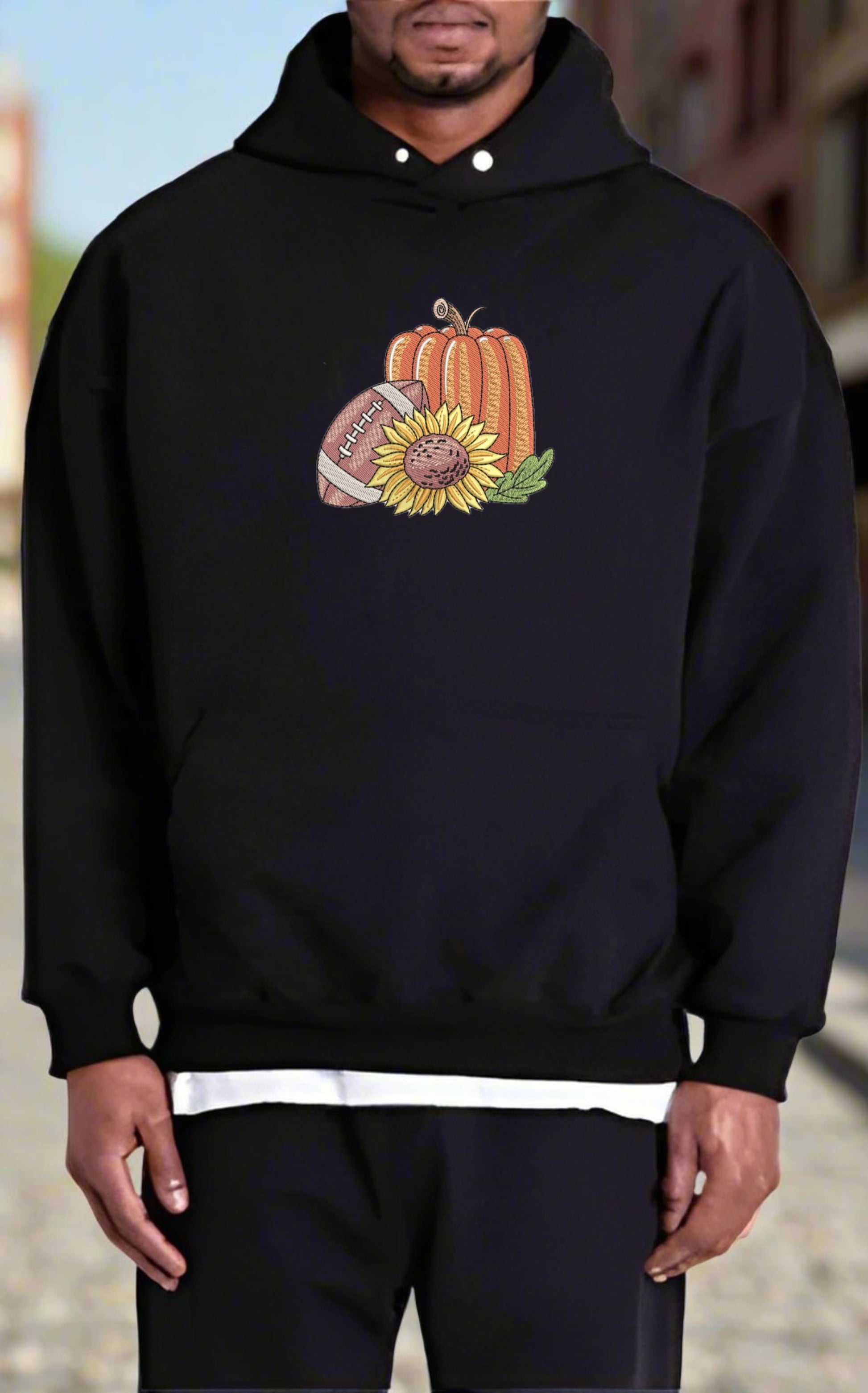 Person wearing a black hoodie with a pumpkin, sunflower, and football design.