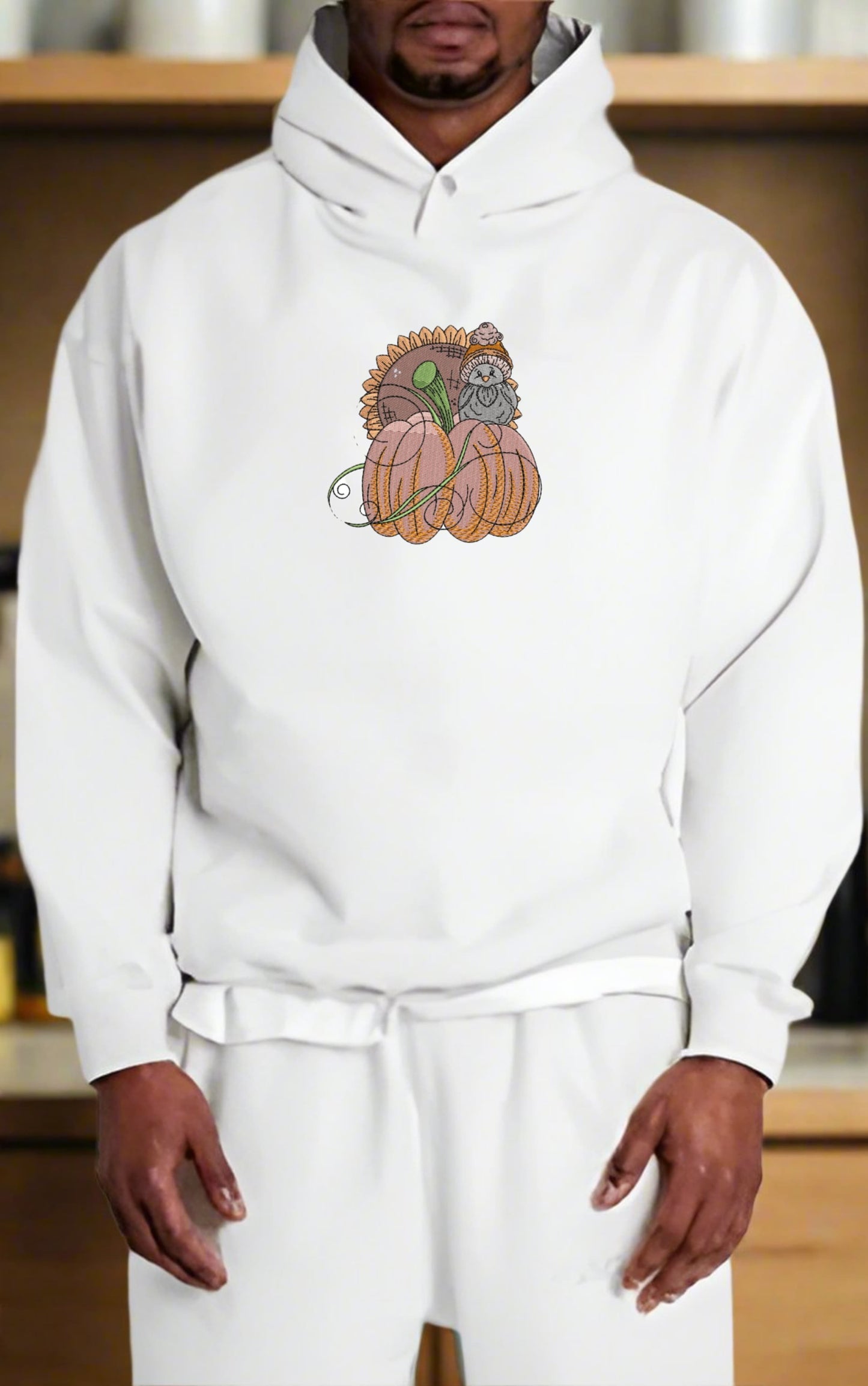 Person wearing a white hoodie with a  Pumpkin Bird & Sunflower Embroidery Design on a wooden shelf background