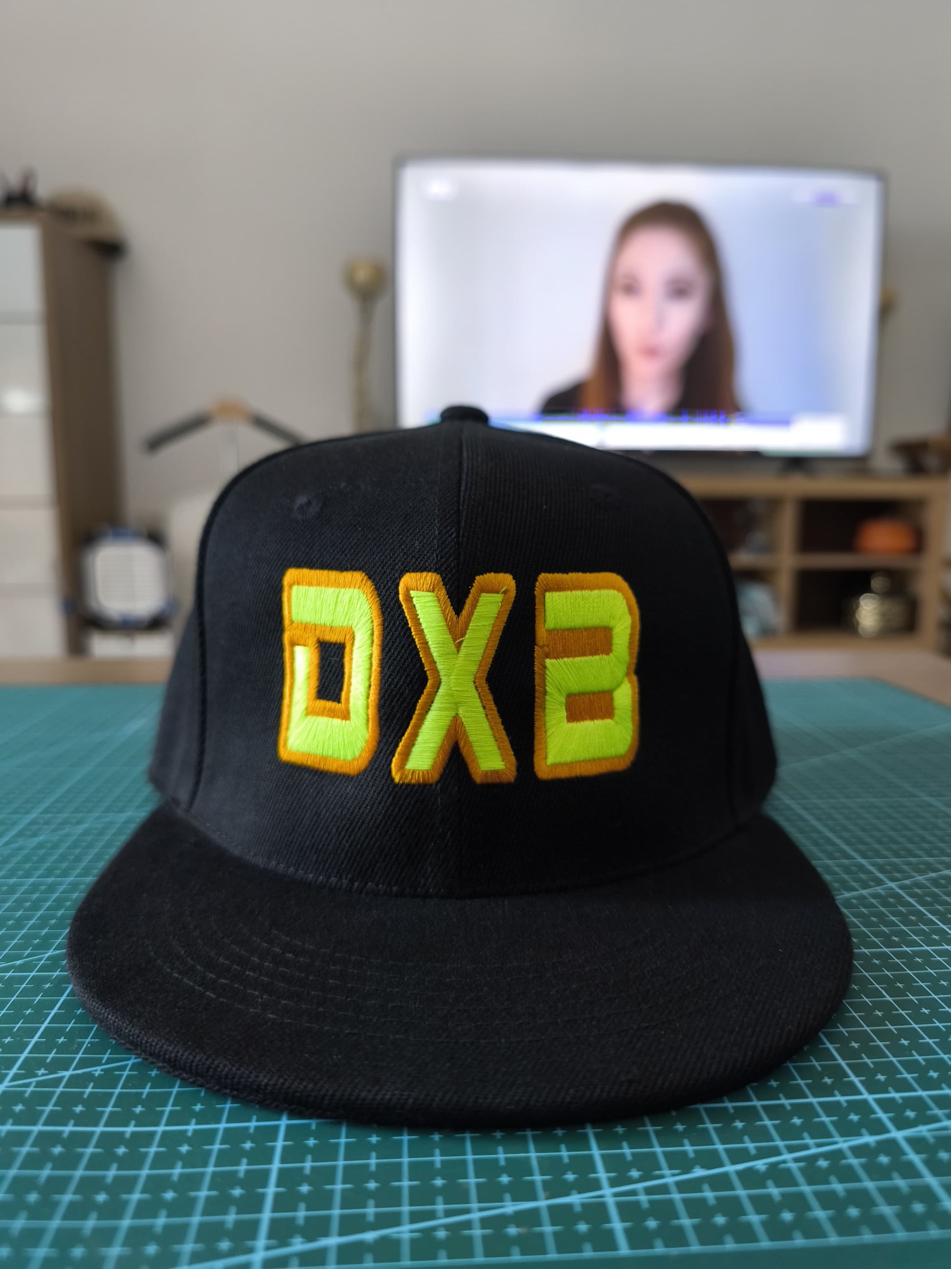 A black baseball cap with raised yellow 3D embroidery letters 'DXB' on the front.