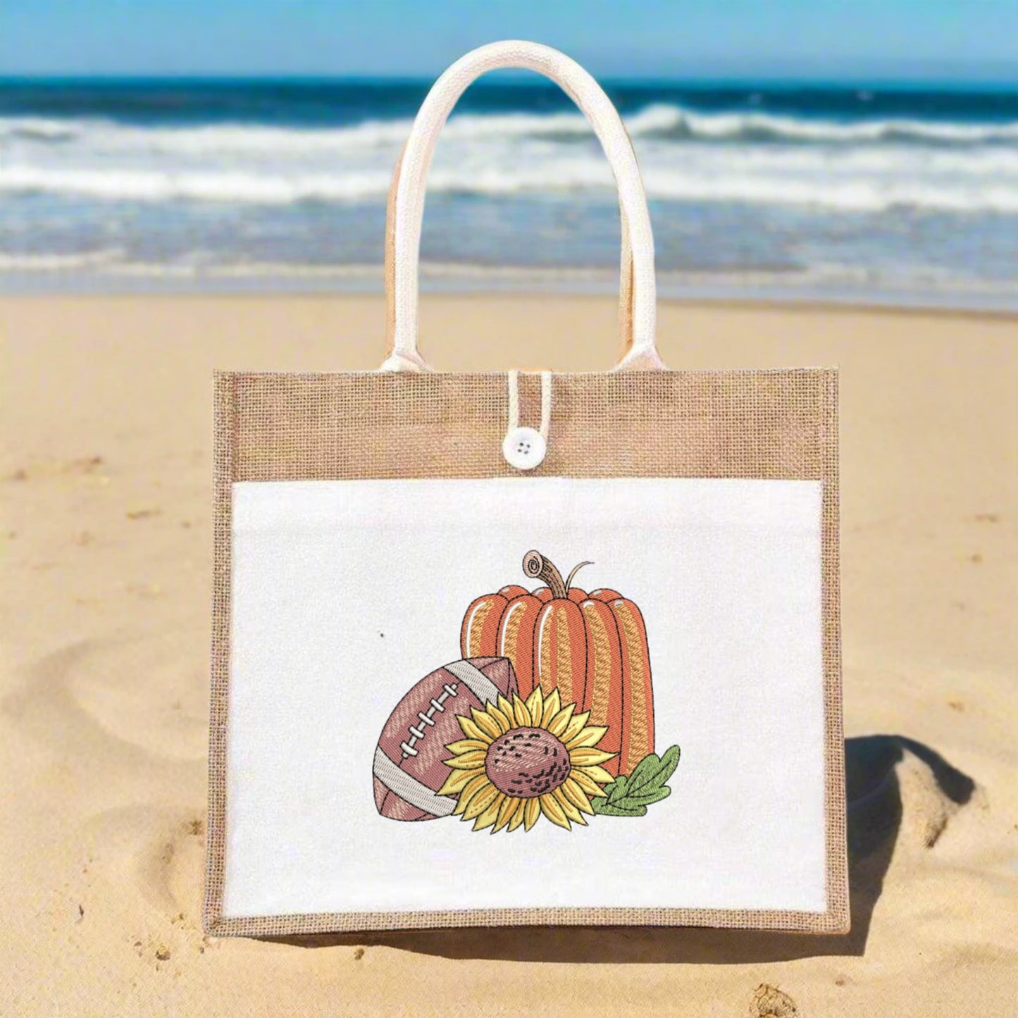 Jute bag with pumpkin, football, and sunflower design on a sandy beach.