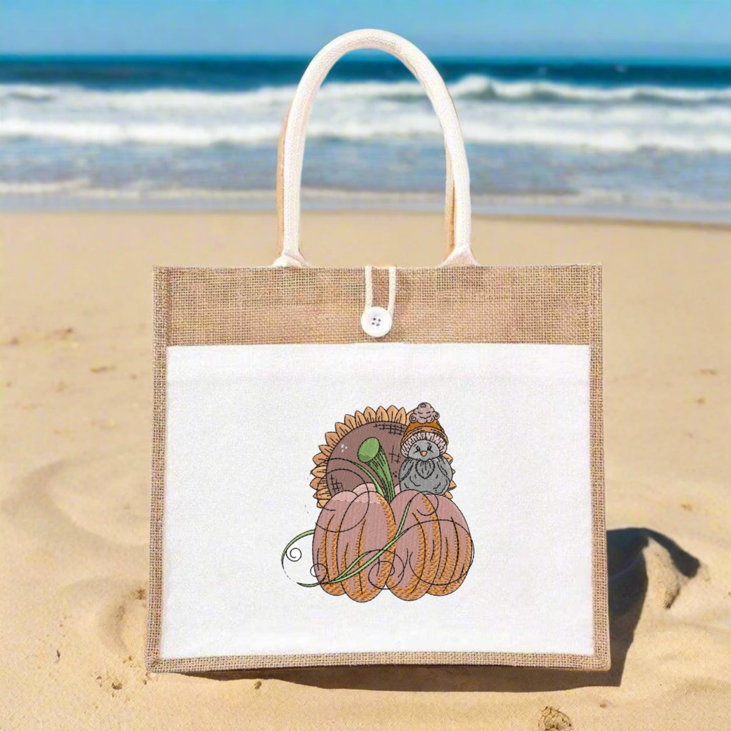 Jute bag with a pumpkin and owl design on a sandy beach with ocean in the background