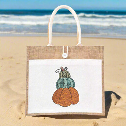 Tote bag with pumpkin design on a sandy beach with ocean in the background