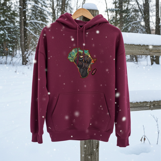 Burgundy hoodie mockup featuring an embroidered raised fist over an Africa map design on the chest, displayed outdoors in a snowy forest setting.