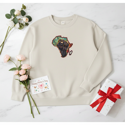 Mint green sweatshirt featuring an Africa map with a raised unity fist embroidery-style design, styled flat lay with roses, a gift box, and a Mother’s Day card.