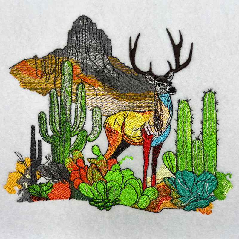 Embroidered desert landscape featuring a deer with antlers, cacti, succulents, and a mountain backdrop stitched on light fabric.