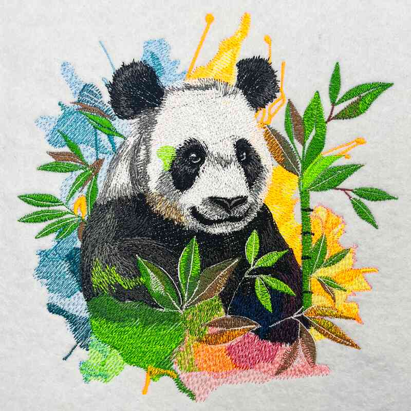 Close-up of an embroidered panda surrounded by bamboo leaves with colorful paint-splash style accents on a light fabric background.
