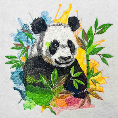 Close-up of an embroidered panda surrounded by bamboo leaves with colorful paint-splash style accents on a light fabric background.