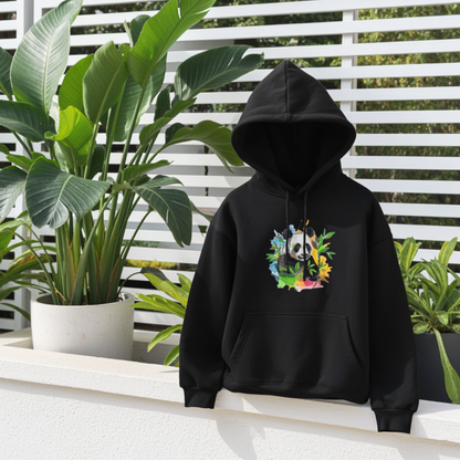 Black hoodie mockup featuring an embroidered panda with bamboo leaves and colorful splash accents on the chest, styled outdoors on a terrace with potted green plants.
