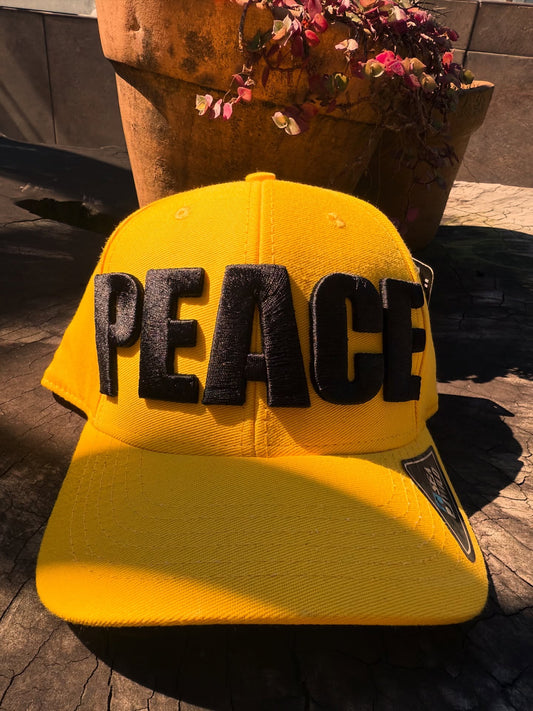 Yellow cap with 'PEACE' in black letters on a textured surface.