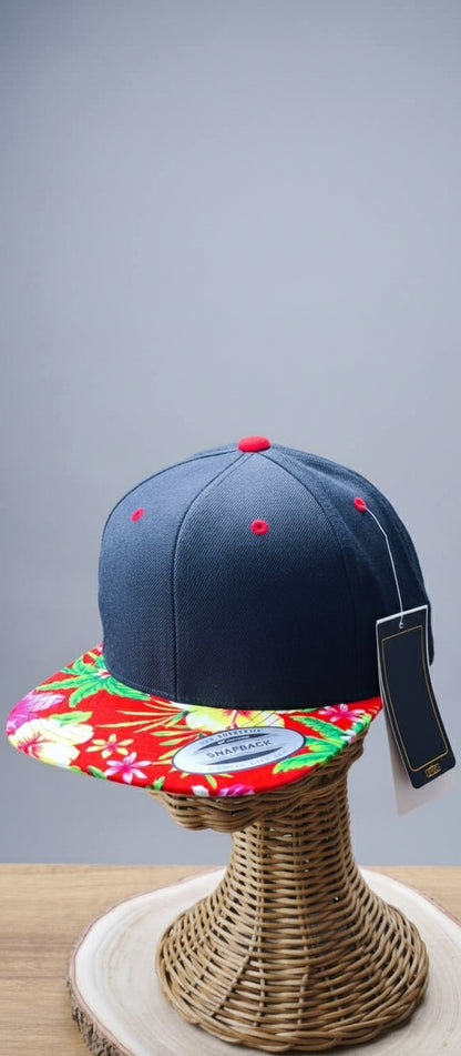 Black cap with red buttons on a colorful floral visor, displayed on a woven stand.