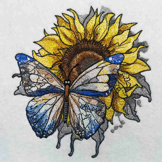 Close-up of an embroidered blue butterfly in front of a yellow sunflower, stitched on light fabric.