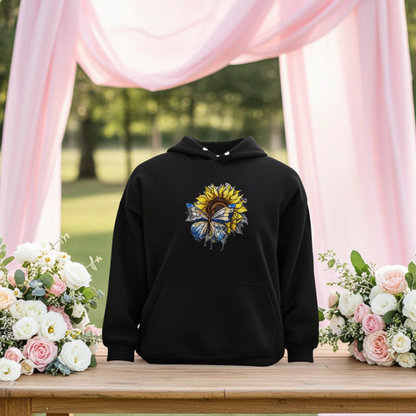 Black hoodie mockup featuring an embroidered blue butterfly and sunflower design on the chest, styled outdoors with pink drapes and floral arrangements.






