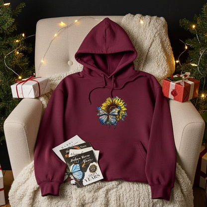 Burgundy hoodie mockup featuring an embroidered blue butterfly and sunflower design on the chest, styled on a cozy armchair with holiday lights and wrapped gifts.






