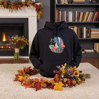 Black hoodie mockup featuring an embroidered blue dragon surrounded by flowers on the chest, styled indoors by a fireplace and bookshelf with autumn leaves and floral arrangements.