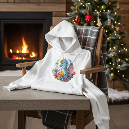 White hoodie mockup featuring an embroidered blue dragon surrounded by flowers on the chest, styled on a chair by a lit fireplace with a decorated Christmas tree in the background.
