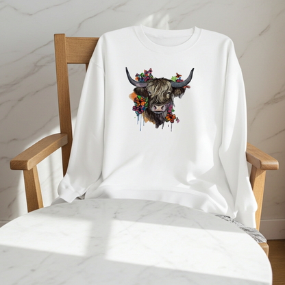 White sweatshirt draped on a wooden chair in a bright minimalist room, featuring a floral highland cow embroidery design on the chest with colorful flowers and long horns
