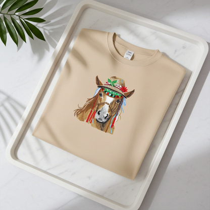 Soft beige sweatshirt neatly folded on a white marble tray, featuring colorful boho horse embroidery with a decorated hat, with leaf shadows in the background