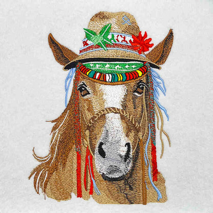 Close-up of an embroidered horse head wearing a decorated western hat with colorful bands and accents on a light fabric background.