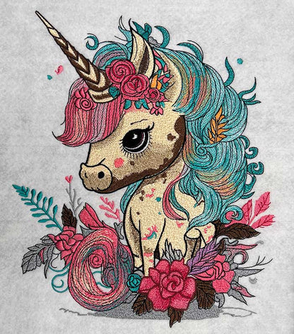 Close-up of an embroidered unicorn with a teal and pink mane, horn, and floral accents, stitched on a light fabric background.