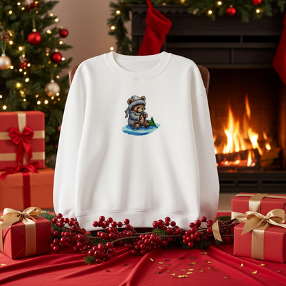 White sweatshirt displayed in a festive holiday setting with fireplace and Christmas tree, featuring a small moonlit bear embroidery wearing a winter hat, surrounded by wrapped gifts and red berries