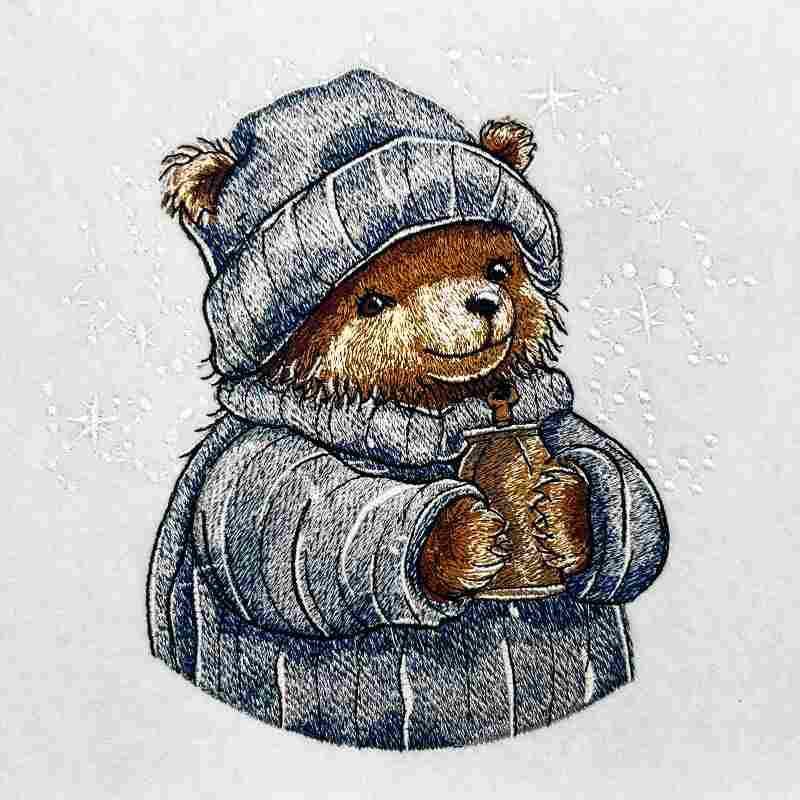 Close-up of an embroidered bear wearing a knit hat and scarf, holding a warm drink, stitched on light fabric.