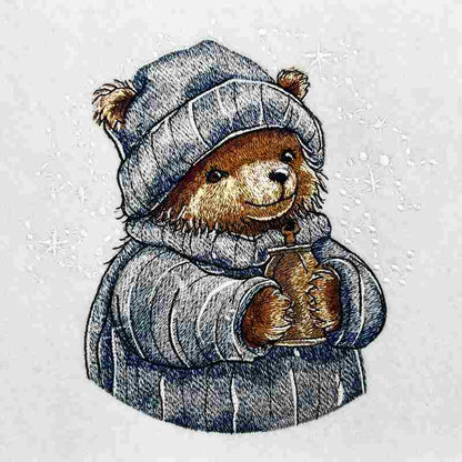 Close-up of an embroidered bear wearing a knit hat and scarf, holding a warm drink, stitched on light fabric.