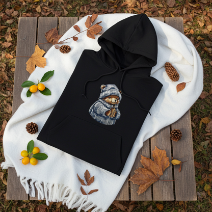 
Black hoodie mockup featuring an embroidered bear in a knit hat and scarf holding a warm drink, styled with autumn leaves, pinecones, a white scarf, and small orange fruits.