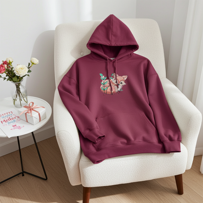 Maroon hoodie featuring a cute woodland fox embroidery-style design, styled on an armchair with flowers and a gift on a side table.