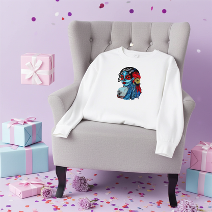 White sweatshirt laid flat on a lavender background with confetti and gift boxes, featuring a colorful sugar skull muse embroidery portrait with red and blue details on the chest