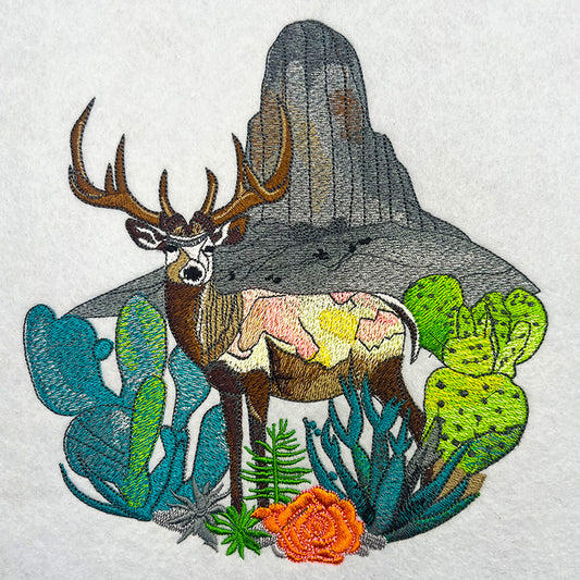 A jute tote bag with intricate embroidery of a mountain buck among floral and mountainous terrain.