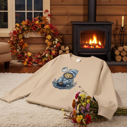 Beige sweatshirt displayed indoors in a cozy candlelit setting, featuring a moonlit sloth embroidery wearing a blue winter hat, with a fireplace, candles, autumn leaves, and flowers in the background