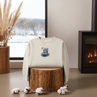 Mint green sweatshirt displayed on a wooden stump indoors near a fireplace and snowy window view, featuring a moonlit sloth embroidery wearing a cozy hat, styled with cotton stems and dried grasses