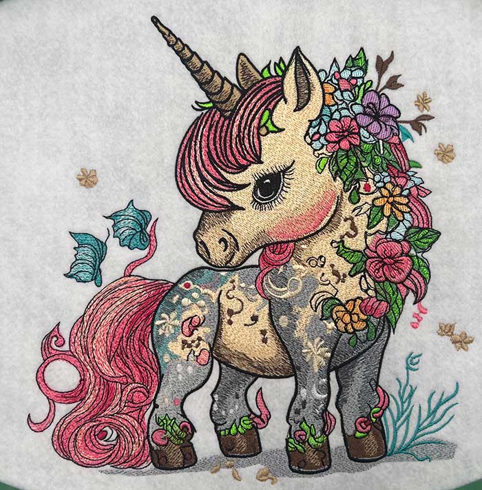 A detailed embroidered image of a unicorn with floral patterns and a moonlit background.