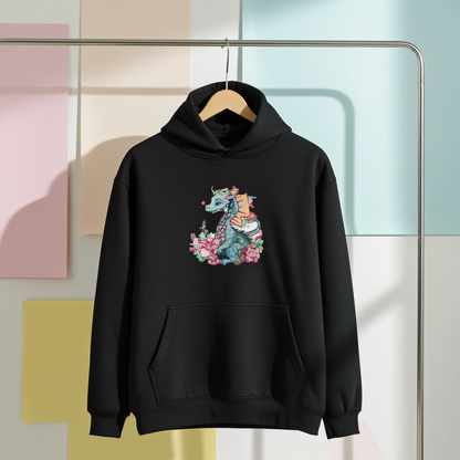 Black hoodie mockup featuring an embroidered teal dragon with orange wings and pink flowers on the chest, hanging on a clothing rack against a pastel studio backdrop.