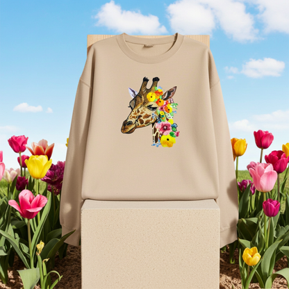 Soft beige sweatshirt hanging on a wooden hanger outdoors, featuring a giraffe head embroidery with colorful floral accents, styled with blooming tulips and a blue sky background