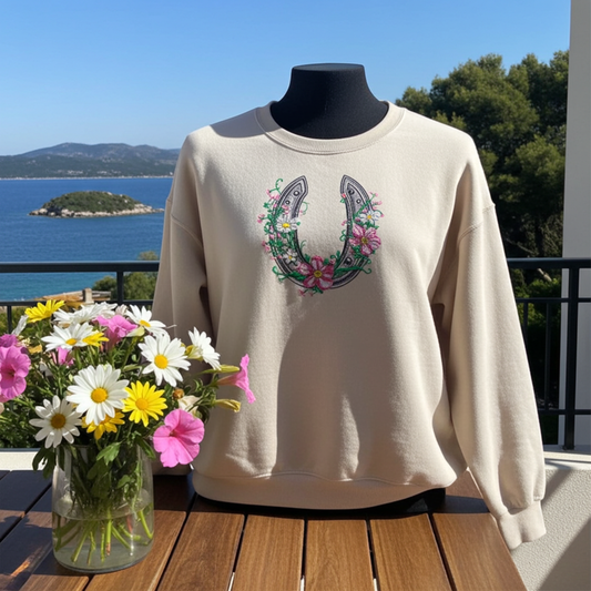 Mint green  unisex crewneck sweatshirt with floral horseshoe embroidery design, displayed on mannequin on balcony with ocean view and bouquet of flowers.