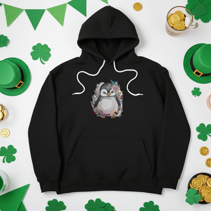 Black hoodie mockup featuring an embroidered cute penguin with floral accents on the chest, styled flat lay on a white background with green shamrocks, green leprechaun hats, bunting flags, and gold coins.