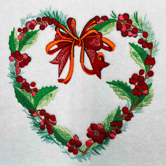 Embroidered heart-shaped wreath design with red and green elements on a white background.