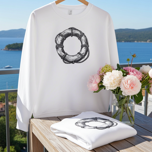 White sweatshirt featuring a lifebuoy ring embroidery-style design, displayed outdoors on a balcony with ocean views and a vase of flowers on a table.